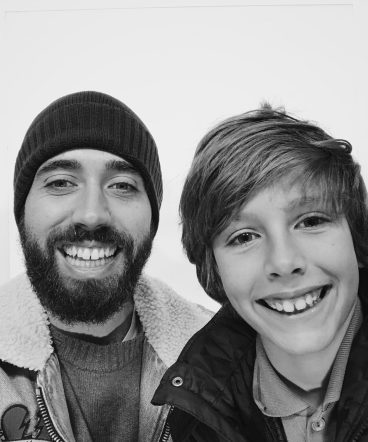 Black and white photograph of a smiling father and son inside a photo booth.