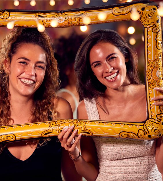 Female Friends Having Fun Posing With Photo Booth Photo Frame At Party In Bar