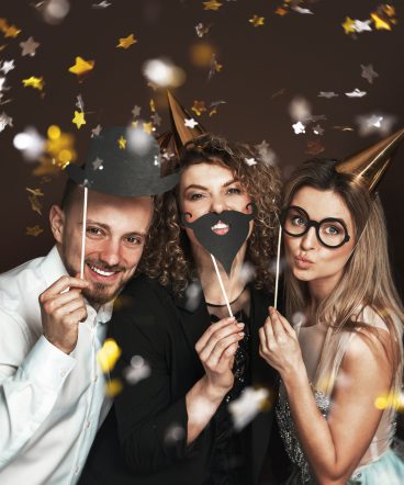 Happy people wearing party hats and using funny photo booth props are celebrating a holiday