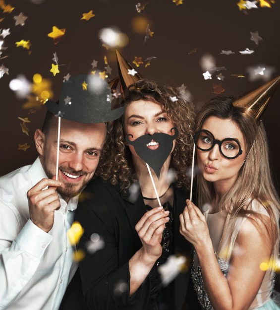 Happy people wearing party hats and using funny photo booth props are celebrating a holiday