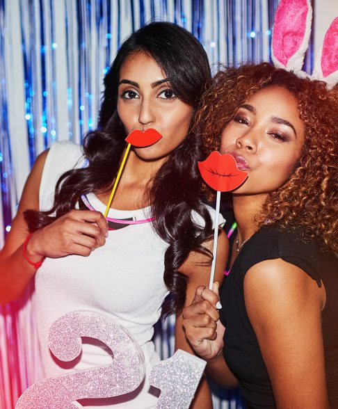 Shot of two beautiful young women having fun with props in a photobooth